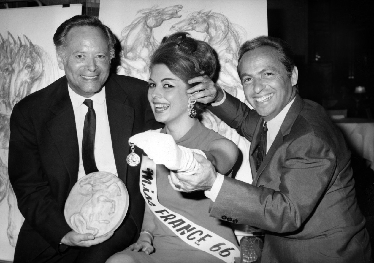 Rene Bollinger (balra) és Guy Lux Entourent Monique Boucher „Miss France” annak, akinek éppen átadtak egy „Talisman Du Turfiste” kulcstartót a Bollingers vászon megnyitásakor 1966. július 12-én. alkotó: Unknown