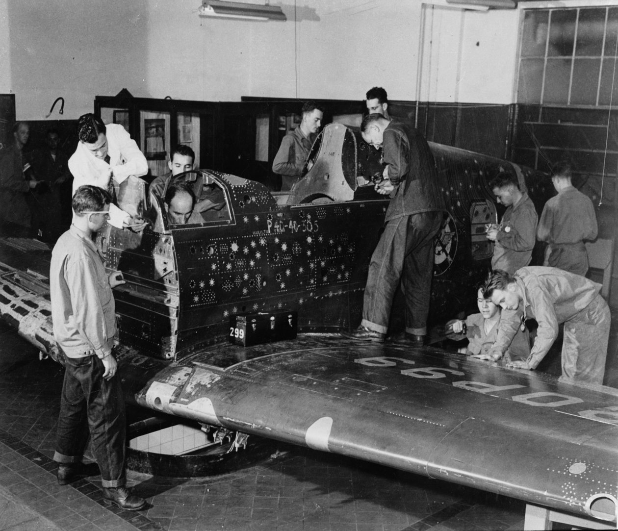 A katona gyakornokok a "Flying Patch"-en dolgoznak, egy Curtiss "Warhawk" vadászrepülőgépen, hajtómű vagy farok szerelvény nélkül, szimulált golyónyílásokkal és foltokkal, 1942 körül alkotó: American Photographer