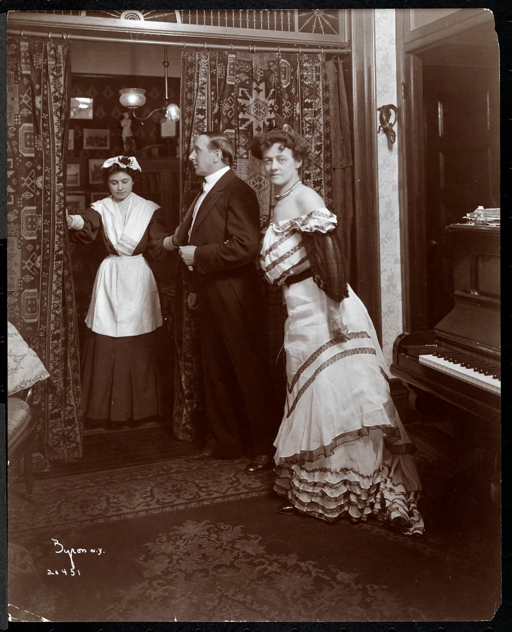 Egy hivatalosan öltözött férfi és nő, és egy háztartási alkalmazottnak tűnő egy zongoraszobában, 1905 (ezüst zselatin nyomat) alkotó: Byron Company