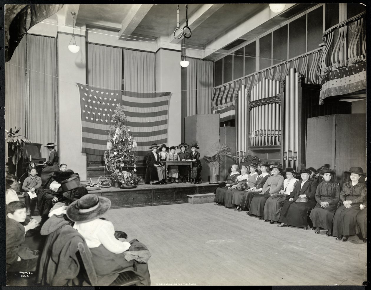 Emberek a New York-i Vakok Egyesületének előadótermében karácsonyfával és emberek, akik valószínűleg egy színpadi jelenetet adnak elő orgonával, 1920 (ezüst zselatinos nyomat) alkotó: Byron Company