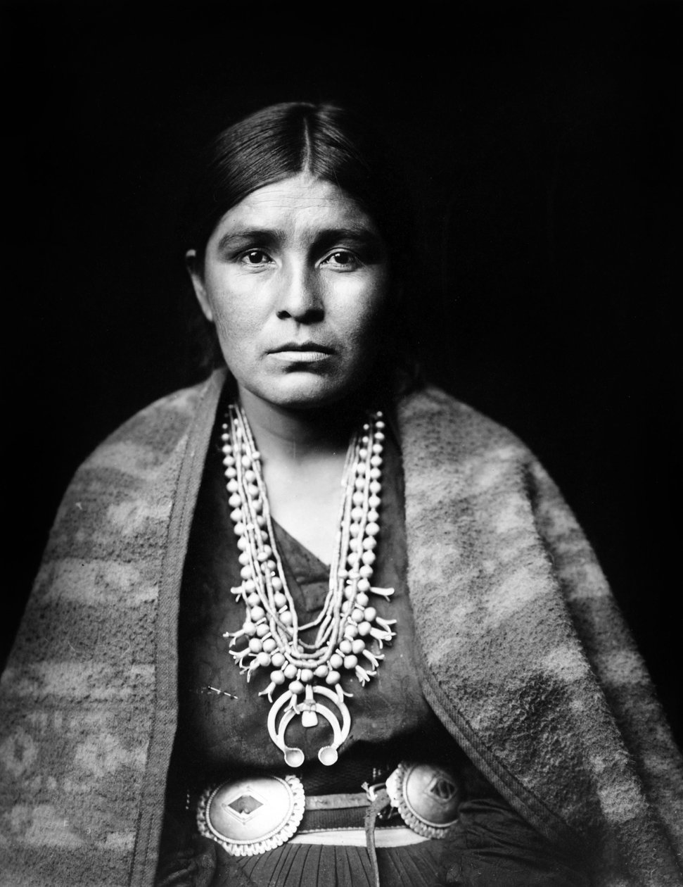Navajo nő ezüst squash blossom nyakláncot, kagylóövet, vállra terített takarót visel, c. 1904, fénykép Edward S. Curtis alkotó: Edward Sheriff Curtis