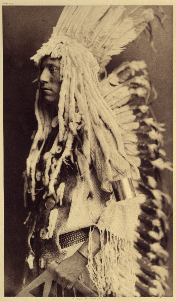 Öreg ember, Piegan. A fiatal férfiak egyetlen nyilvános ünnepséget sem hagynak ki, hogy felvegyék harcos apjuk ruháját. A kép az Edward S. Curtis (1868-1952) által az észak-amerikai indiánokról szóló enciklopédiának 6. kötetéből származik, elől alkotó: Edward Sheriff Curtis