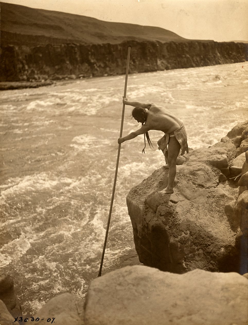 Tlakluit indián, sziklán állva, halászik merítőhálóval, 1910 körül (fekete-fehér fotó) alkotó: Edward Sheriff Curtis