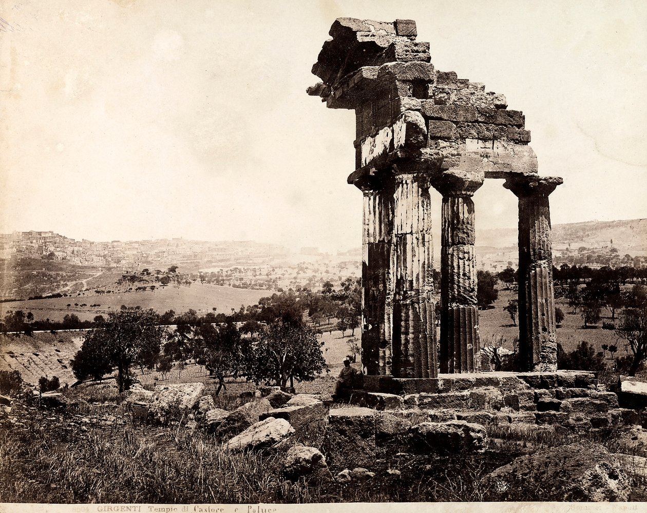 Nézet a fennmaradó négy oszlopról, amelyek Castor és Pollux templomának anablatúráját támasztják alá a Valle dei Templiben, Agrigentoban. A háttérben a város panorámája látható alkotó: Giorgio Sommer