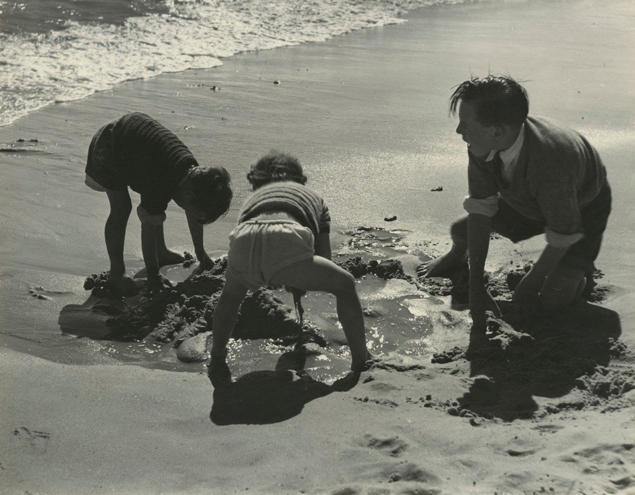 Három gyerek játszik a homokkal a strandon. alkotó: Godfrey Macdominic