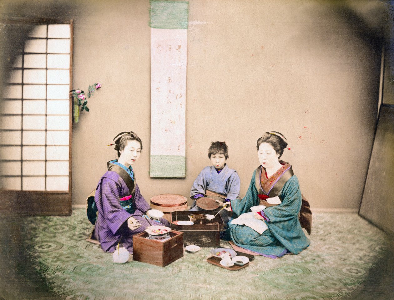 Két nő és egy gyerek egy szőnyegen ülve ebédelnek, 1890 körül (kézzel színezett fotó) alkotó: Japanese Photographer