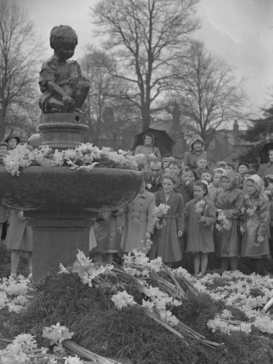Gyermekek nárciszcsokrokat helyeznek a szökőkútra, amelynek tetején szobor áll alkotó: Joseph Hardman