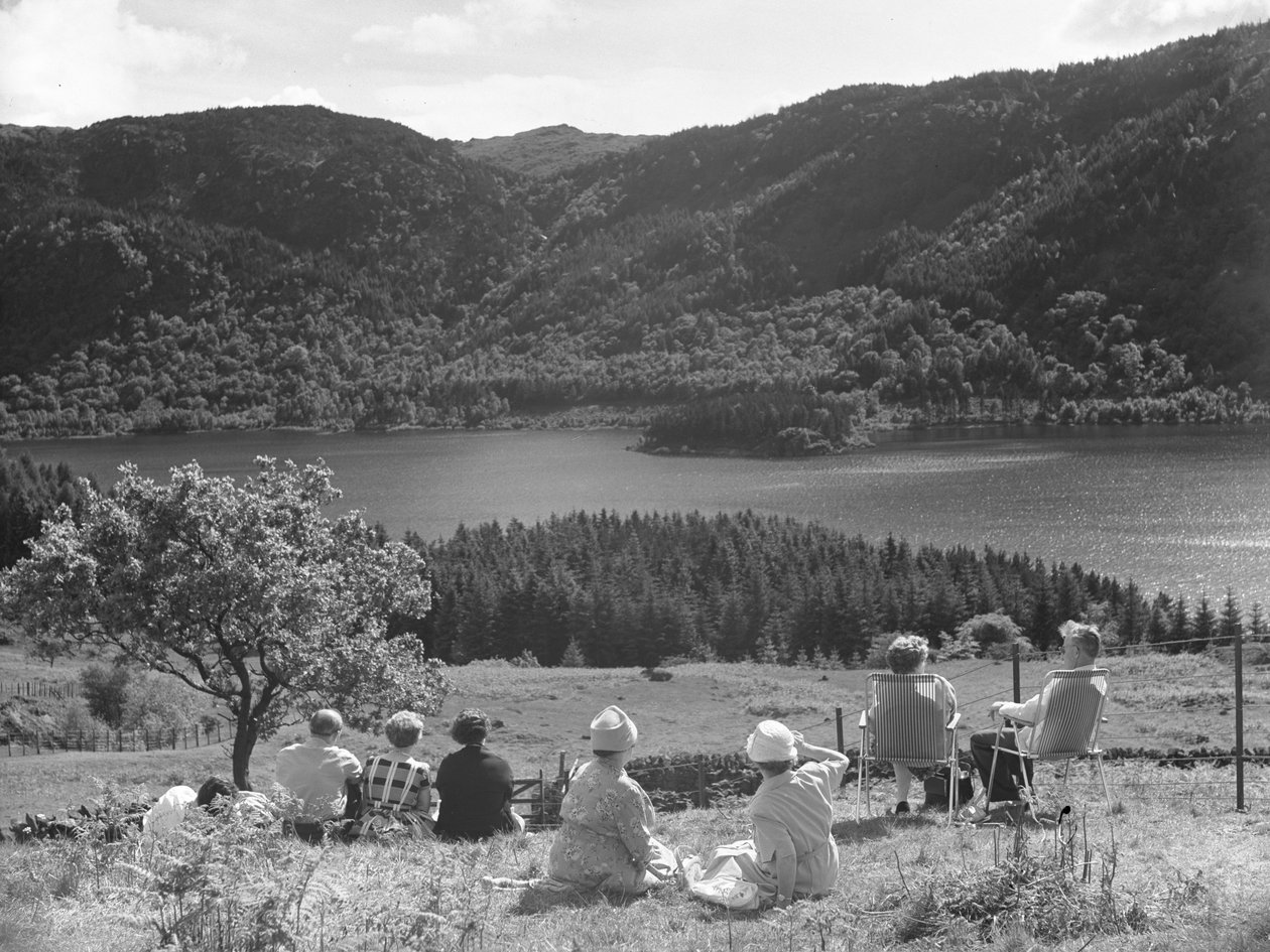 Emberek csoportja ül a fűben vagy nyugágyon, Thirlmere kilátását nézve alkotó: Joseph Hardman