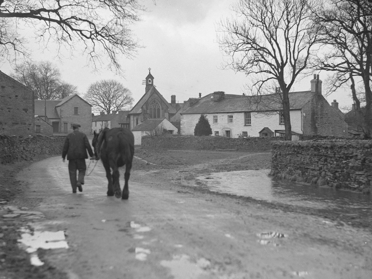 Férfi vezeti lovát a kamerától távolodó úton a falu épületei és a templom felé; építészet; vallás; egyházi épületek; alkotó: Joseph Hardman