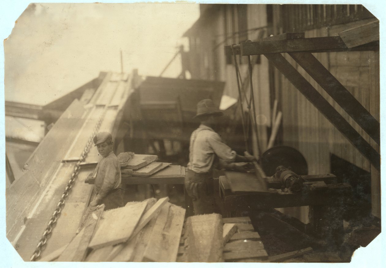Charlie McBride 12 évesen 10 órán át fát szed ki egy csúszdából a Miller und Vidor Lumber Company-nál, Beaumont, Texas, amiért 50 centet keres, míg a másik fiú egy őrzés nélküli körfűrészen fűrészeli, 191 alkotó: Lewis Wickes Hine