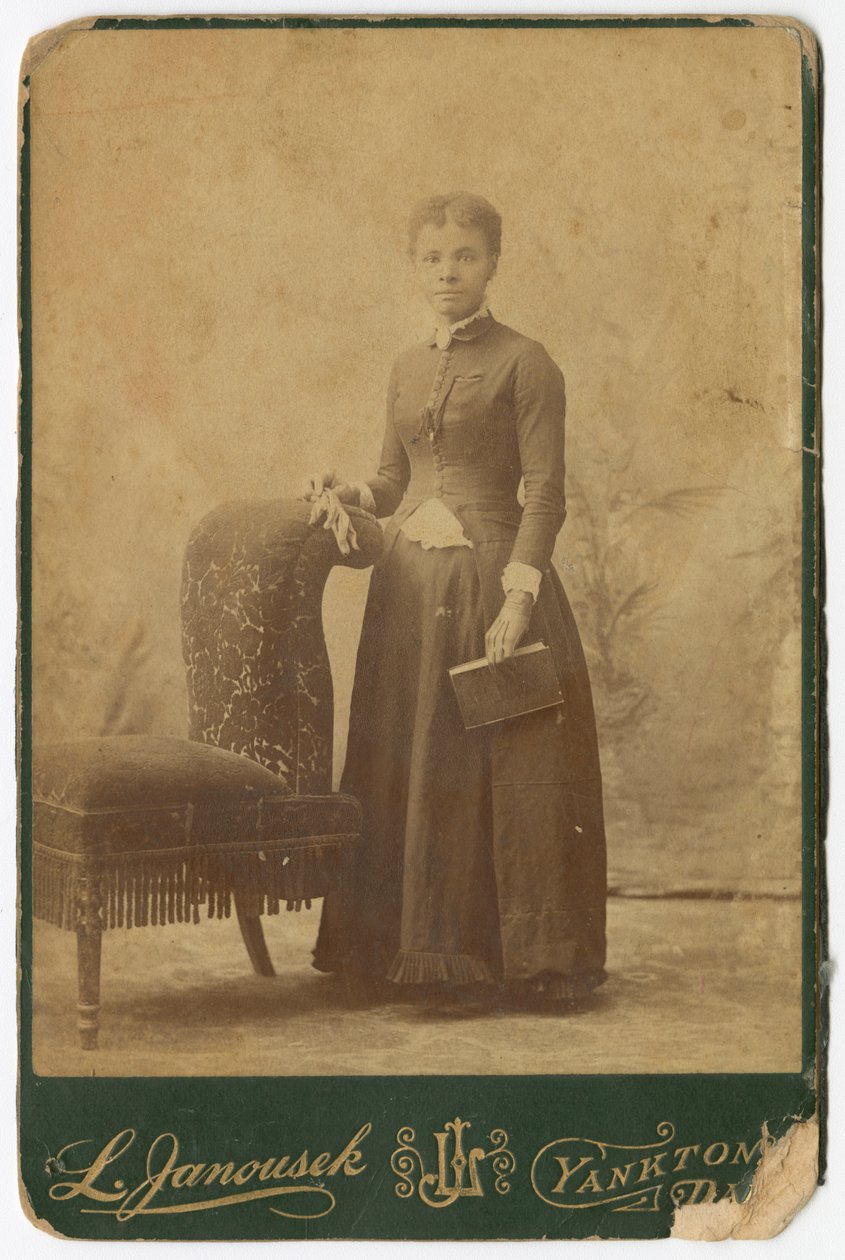 Fénykép egy nőről, aki egy szék mellett áll, és könyvet tart a kezében, 19. század végén. alkotó: Louis Janousek