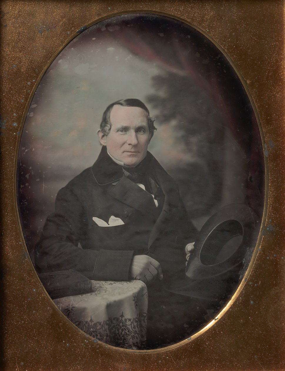 Kabátot és kesztyűt viselő férfi, kalapot tart, festett kültéri háttér előtt ül, 1840-es évek. alkotó: Samuel Broadbent Jr..