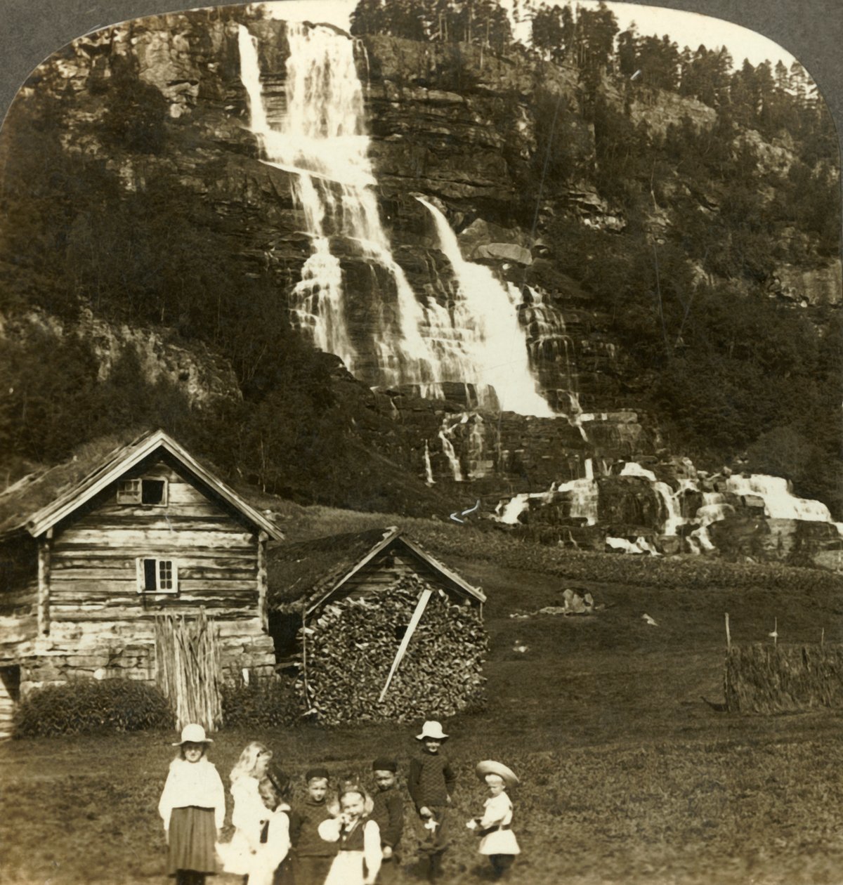 Gyerekek játszanak egy farmer mezőn teraszos Tvinde-vízeséssel, Vossevangen, Norvégia, 1905. alkotó: Unbekannt