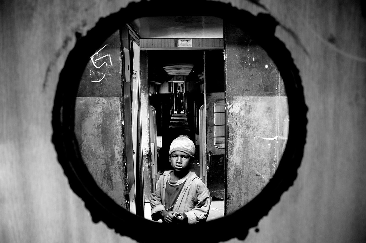 Egy utcagyerek portréja, aki egy vonat rekeszének ajtónyílásán keresztül látható a kamalapuri pályaudvaron Dakkaban, Bangladesben. 2007. január 5. alkotó: Unbekannt Unbekannt