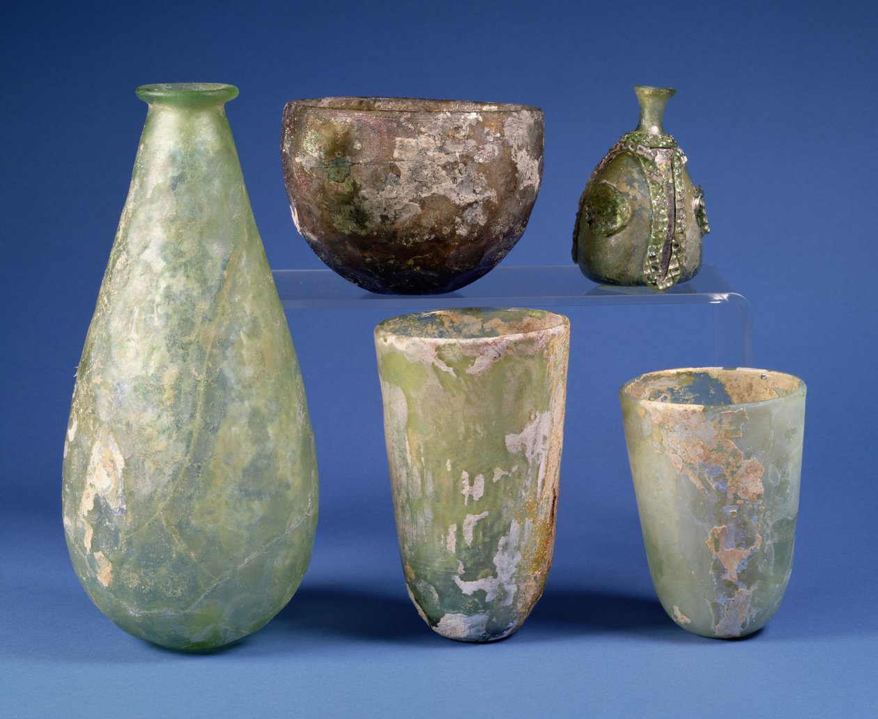 Az óramutató járásával megegyező irányban balról: körte alakú zöld üveglombik, Sasanian, Kr.u. 3-7. század; halvány borostyánszínű üvegtál, Sasanian, Kr.u. 5-6. század; Iszlám zöld, körte alakú üveg lombik, i.sz. 8-12. század körül; két iszlám zöld üvegpoh alkotó: Unbekannt