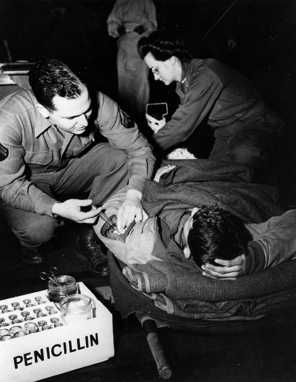 Második világháború (1939-1945) – II. világháború (II vagy WW2): Luxemburg 1945. február: Az Egyesült Államok hadseregének evakuációs kórházában egy orvos (ápolónő) penicillint ad be egy sérült katonának, hogy elkerülje a fertőzést, miközben egy nővér kész alkotó: Unbekannt