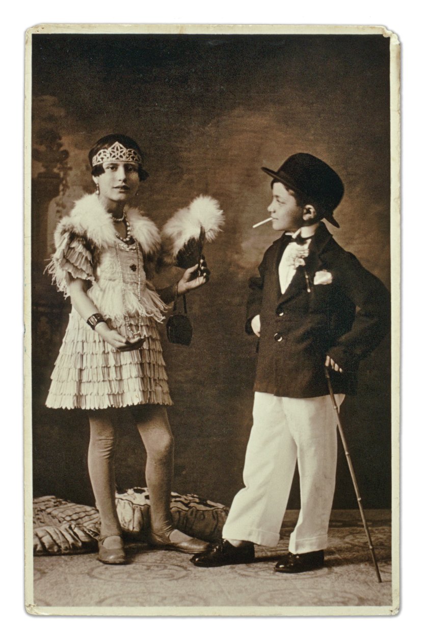 Két felnőttnek öltözött gyermek az 1920-as évek divatja szerint öltözött, a kislány Charleston-ruhát visel, ő pedig öltönyben, bowler-kalapban és cigarettával. Fényképezés alkotó: Unbekannter Künstler