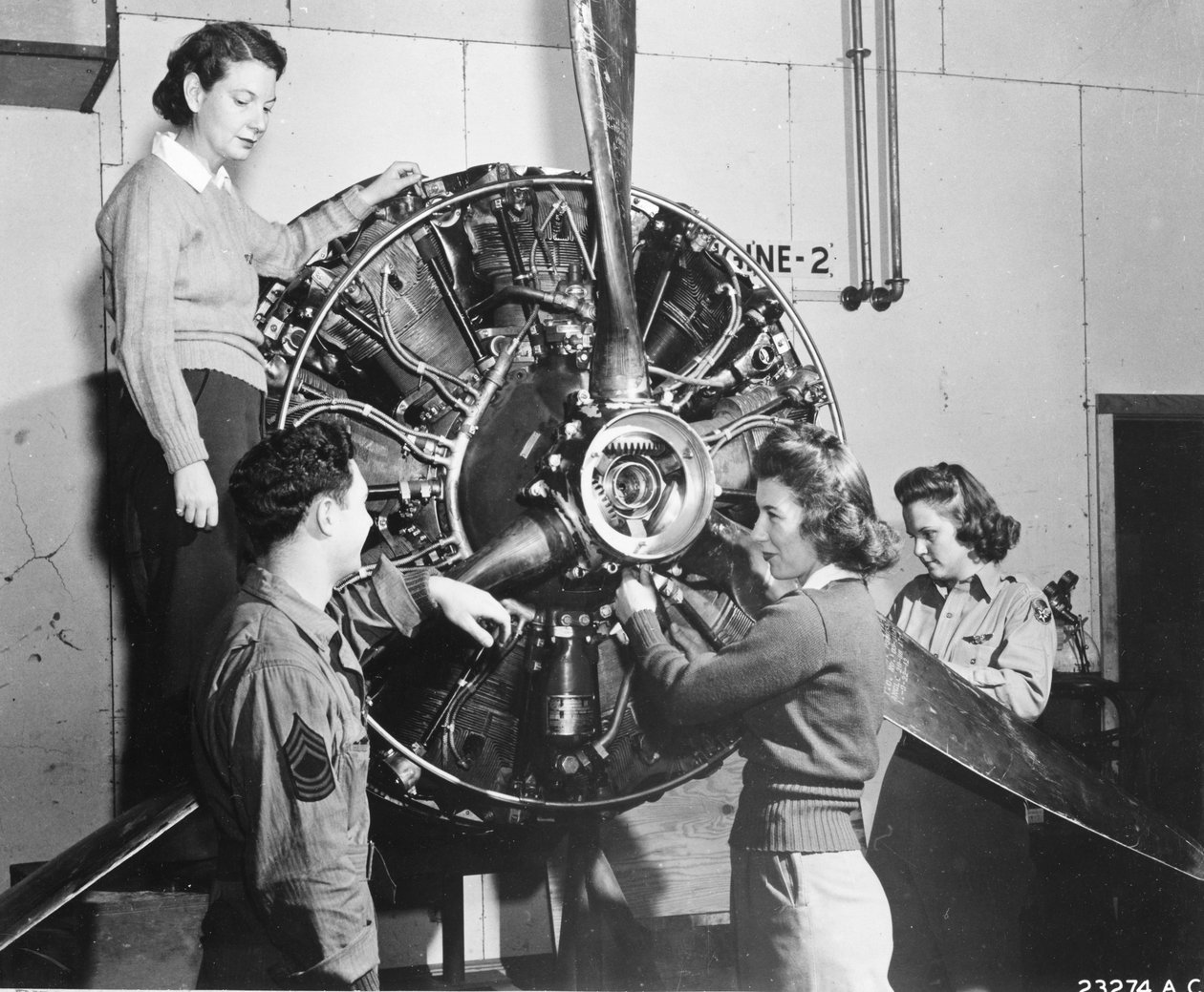 A darazsak megtanulják, honnan származik az erő a B-17 Flying Fortress hajtóművében, miközben részt vesz a B-17 pilótaképzésen a Lockbourne AAB-nál, a propeller mechanizmuson dolgoznak, miközben a legénység vezetője nézi őket (lr): Patricia Bowser, Ann Wal alkotó: Benjamin Baud