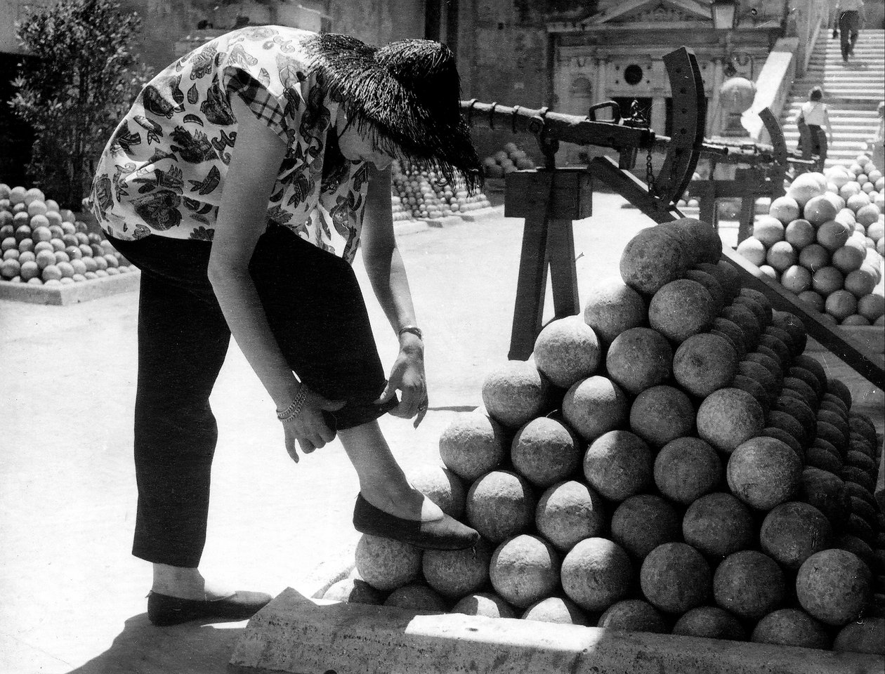 Egy nő megigazítja a nadrágja mandzsettáját, miközben lábát egy halom ágyúgolyón pihenteti a római Angyalvár területén. alkotó: Unknown photographer