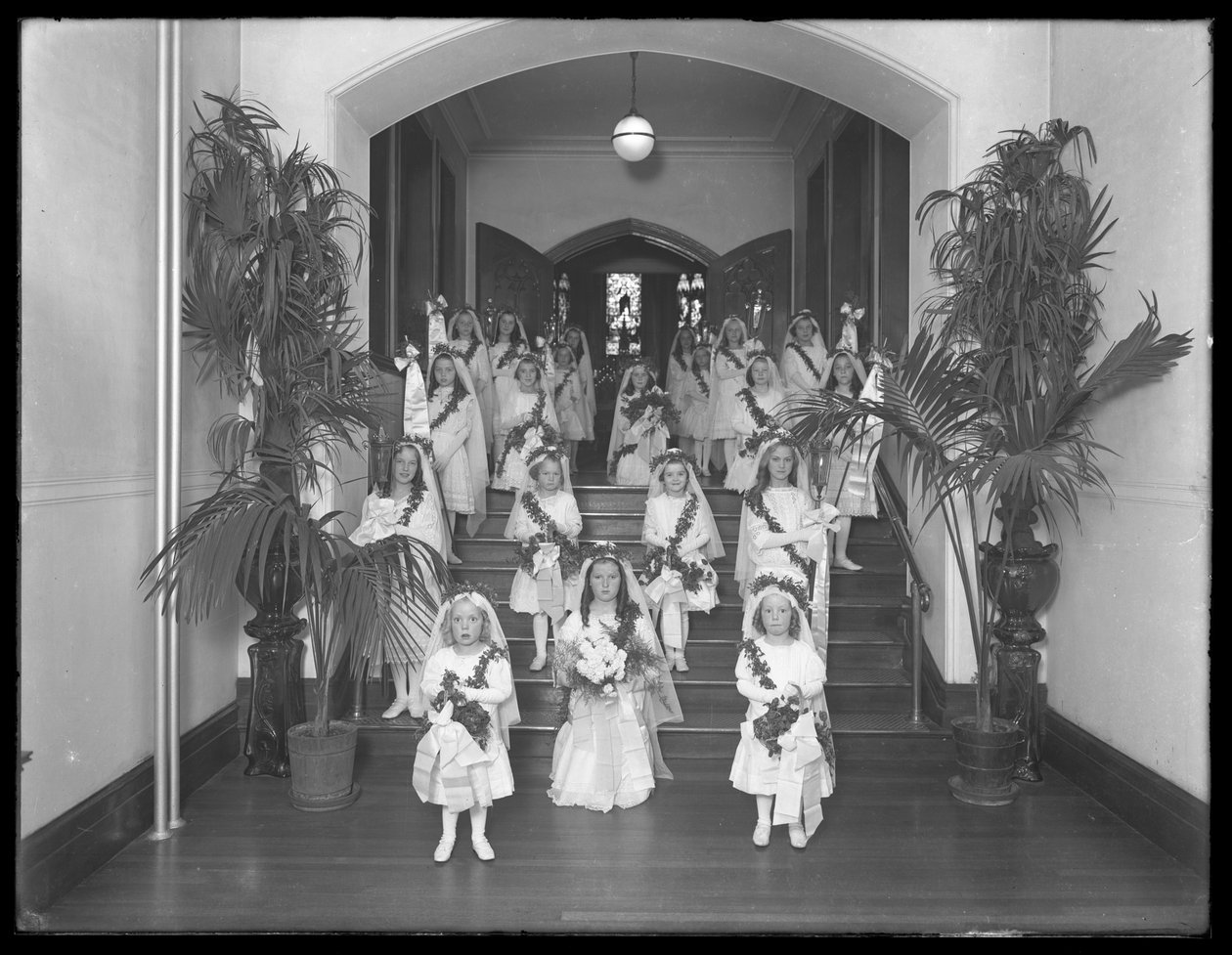 Kislányok a bronxi Kingsbridge-i római katolikus árvamenhelyen, fehér ruhákban, koszorúkkal és füzérekkel térnek vissza a kápolnából, 1914. október 20. alkotó: William Davis Hassler