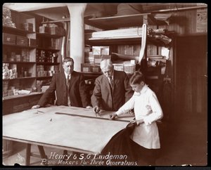 Henry és S.G. Lindeman portréja fiukkal vagy unokájukkal, akik zongorára készült bolti rajzok felett állnak, 1910 (ezüst zselatin nyomat)
