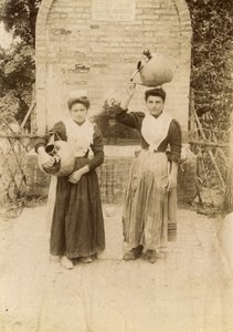 Két fiatal nő hagyományos ruhát visel és terrakotta edényeket cipel kút mellett, Marche, Olaszország, 1910 körül alkotó: Italian Photographer