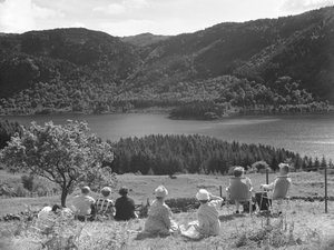 Emberek csoportja ül a fűben vagy nyugágyon, Thirlmere kilátását nézve alkotó: Joseph Hardman