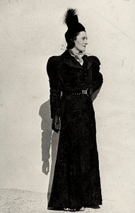 A modell bemutat egy, az olasz "Cicogna" couture-ház által készített cikket, amely egy breitschwanz felöltőből áll, amelyet ékköves csattal ellátott öv fog össze a derekán, és egy kis tollas kalap fátyollal (f/w fotó)