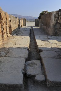 Phaistos minószi régészeti lelőhelye. Széles folyosó vízelvezető csatornával az északi szárny kapuja mögött, amely a központi pályáról nyílik és a Royal Apartments melletti belső udvarhoz vezet. Phaistos, Kréta. alkotó: Minoan