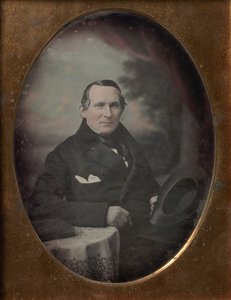 Kabátot és kesztyűt viselő férfi, kalapot tart, festett kültéri háttér előtt ül, 1840-es évek. alkotó: Samuel Broadbent Jr..