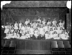 Kislányok csoportja pózolt egy kis színpadon babákat tartva, valószínűleg a római katolikus árva menhelyen, Kingsbridge, Bronx, 1911 körül