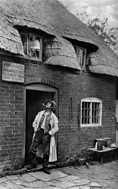 Egy férfi pipázik egy bolt előtt, Worcestershire, 1922. alkotó: A. W. Cutler
