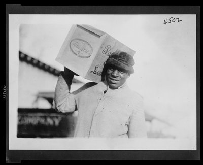 Afro-amerikai férfi, aki egy doboz "Four Roses" whiskyt cipel a vállán, valószínűleg lefoglalta az Egyesült Államok Adóhivatala alkotó: American Photographer