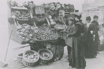 Egy élelmiszerbolt áll a bódéja mellett, miközben egy nőt szolgál ki alkotó: English Photographer