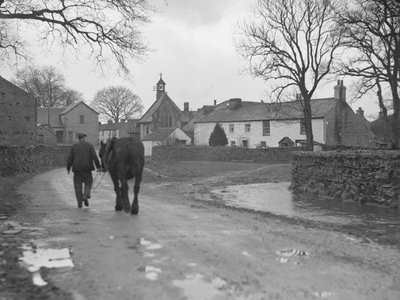 Férfi vezeti lovát a kamerától távolodó úton a falu épületei és a templom felé; építészet; vallás; egyházi épületek; alkotó: Joseph Hardman