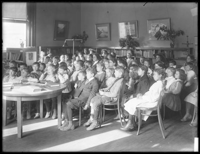 Ülő, hallgató gyerekek a Queens Borough Public Library egy azonosítatlan fiókjának olvasótermében, 1910 körül. alkotó: William Davis Hassler