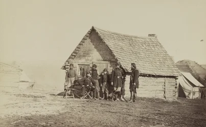 Egy csoport katona és két fiatal férfi, az egyik afroamerikai, a faháznegyed előtt áll, 1861-65
