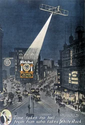 Alkoholreklám „” White Rock””: A New York-i Times Square egyik épületén függő „White Rock” plakátot megvilágító repülőgép. 1912.