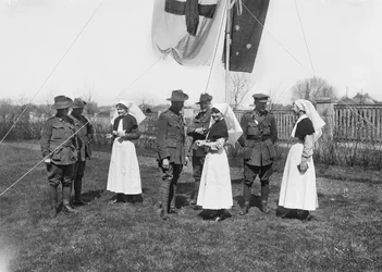A 3. ausztrál baleset-elhárító állomás azonosítatlan tisztjeinek, ápolóinak és embereinek egy csoportja az ausztrál zászlót (Australian Blue Ensign) és a Vöröskereszt zászlót lobogtató rúd alatt gyűlt össze.