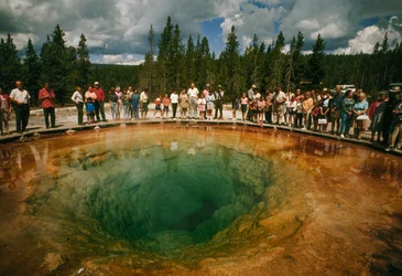 A park látogatói egy kékeszöld, virág alakú termálmedence körül gyűlnek össze. Yellowstone Nemzeti Park