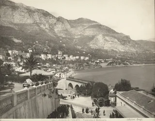 Panorámás kilátás Montecarlóra Monacóban. A jelenet különféle járókelőket mutat be; bal oldalon egy márványkorlát közeli képét látjuk