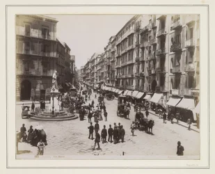 A nápolyi Via Roma látképe szoborral, üzletekkel, lovaskocsikkal és járókelőkkel