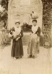 Két fiatal nő hagyományos ruhát visel és terrakotta edényeket cipel kút mellett, Marche, Olaszország, 1910 körül
