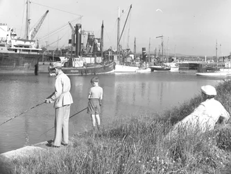 Egy férfi és egy fiú horgászik Glasson Dockban, miközben egy mögöttük ülő hölgy nézi őket, több csónak kikötve áll