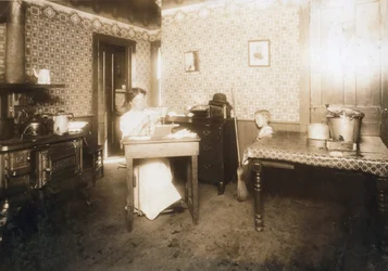 Nő, aki sörtéket helyez a fogkefébe a konyhájában, 1912 körül