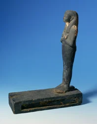 Ptah-Sokar-Osiris figura háromrészes parókával és keresztbe tett karokkal egy téglalap alakú lábazaton, papiruszszelvényt tartalmazó rekesszel (lásd: 83304), egyiptomi, 21-22. dinasztia, Kr.e. 900 körül (fa) (részletesen lásd: 83306)