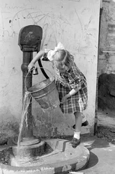 Kislány ürít egy vödör vizet egy szivattyús szökőkútban, 1939. május 9. (fekete-fehér fénykép)