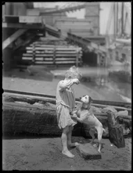 Mezítlábas fiú, valószínűleg William Gray Hassler, kutyával játszik egy folyó vagy tó partján, New York, 1910 körül