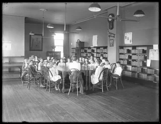 Gyerekek hallgatják a nőt a Queens Borough Public Library egy azonosítatlan fiókjának olvasótermében, 1910 körül.